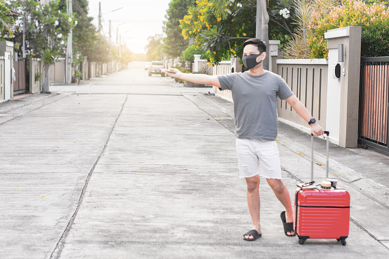 一名戴着流感口罩的男子在街道上拿着行李打手势图片素材