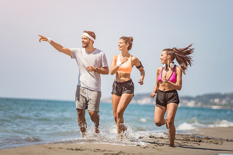 三个年轻的运动朋友一起在海滩上跑步。图片下载