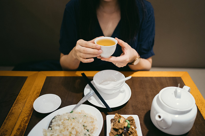 年轻的亚洲女人在中国餐馆吃饭的时候喝着一杯茶图片素材