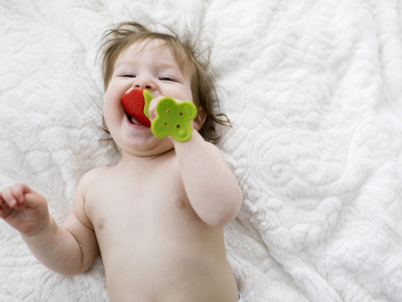 小女孩躺在毯子上咬着草莓玩具图片素材