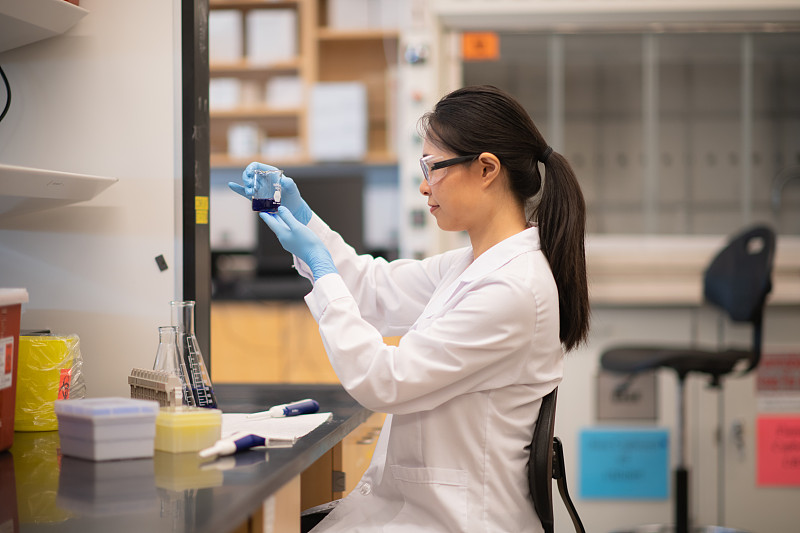 一位亚洲生物化学家正在烧杯中检验一种蓝色化学物质图片下载