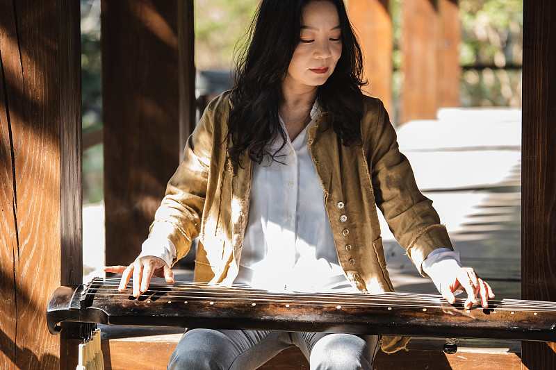 年长的亚洲妇女弹奏中国传统乐器古琴图片素材