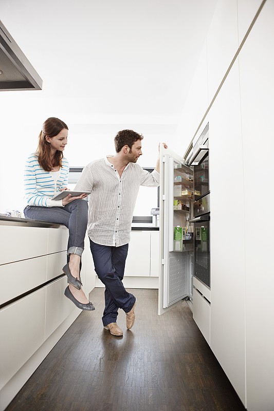 年轻夫妇在厨房里，女人在用平板电脑图片下载