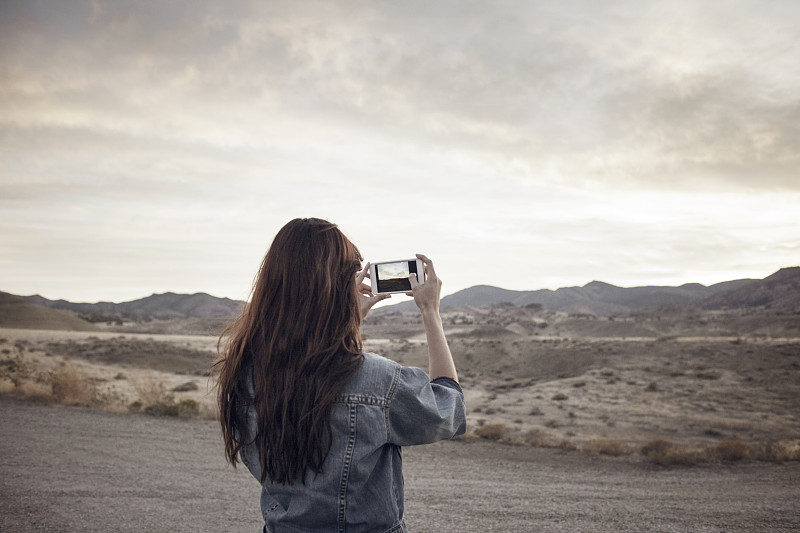 女子站在野外拍摄山景的后视图图片下载