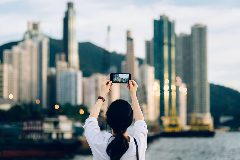 年轻女子在日落时用手机拍摄美丽的城市天际线图片下载