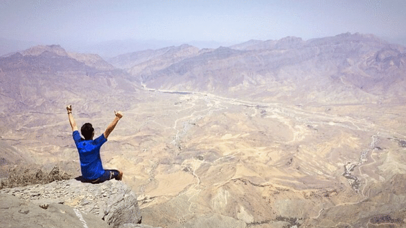 阿曼，在山顶边举起手臂坐着的男人的后视图图片下载