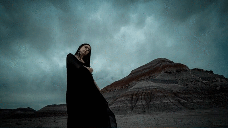 喜怒无常的女人的肖像在长黑衣服附近的大岩层与灰色的云移动头顶图片下载
