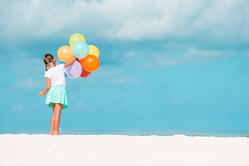 可爱的女孩拿着五颜六色的气球在海滩上图片素材
