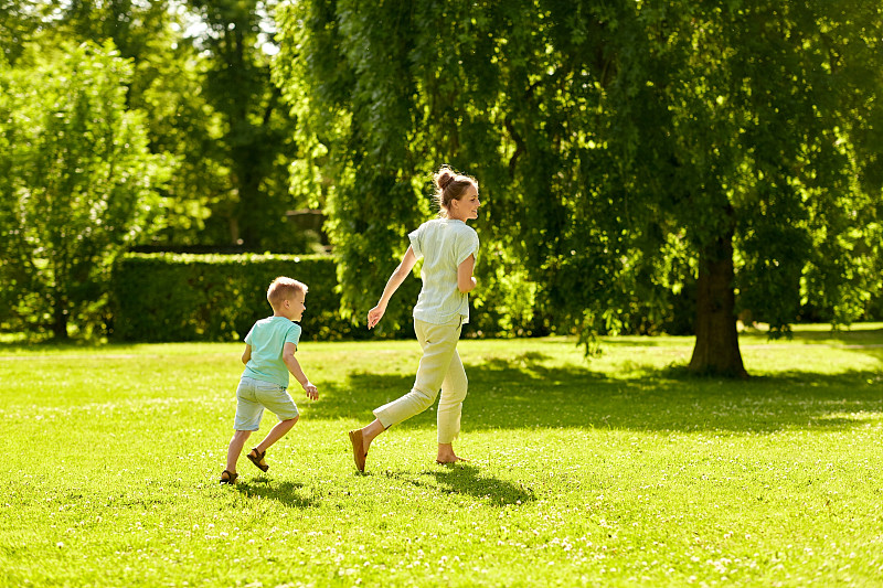 家庭、休闲和人的概念——快乐的妈妈和小儿子在夏季公园里奔跑和玩接球游戏。母亲和儿子在夏季公园玩接球游戏图片下载