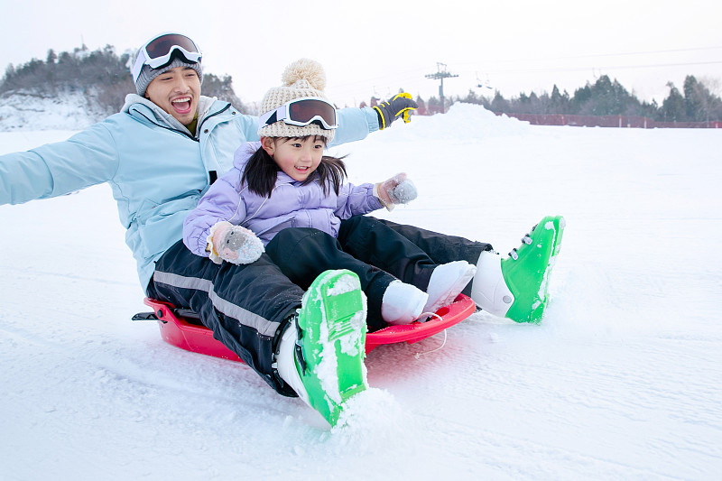 滑雪场上快乐父女坐着雪上滑板滑雪图片素材