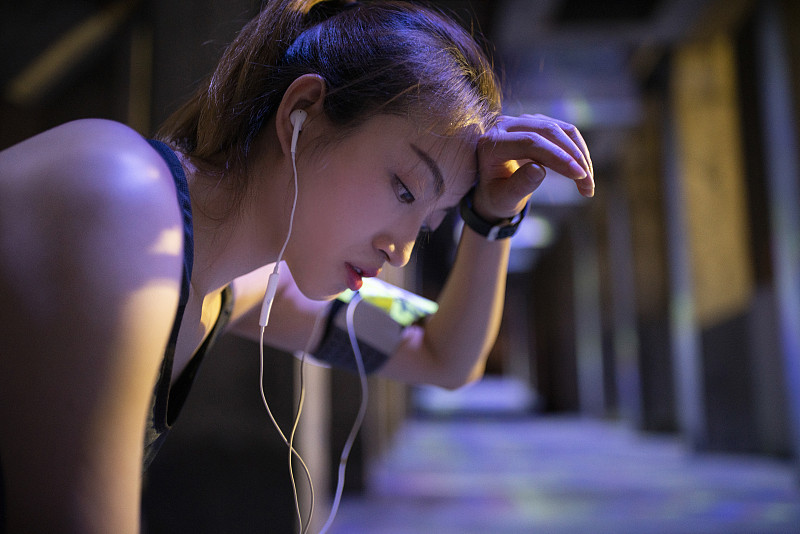 年轻女子夜跑后戴耳机听歌休息图片素材