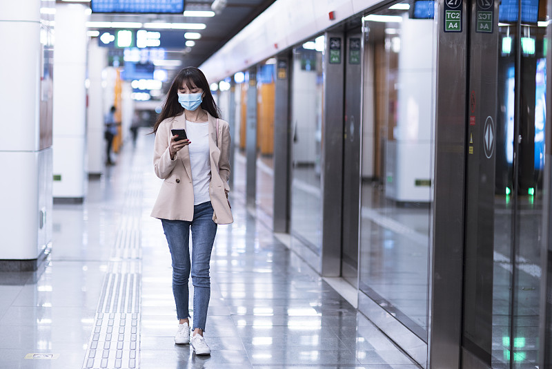 年轻女子戴着防护口罩等候地铁并使用智能手机图片下载
