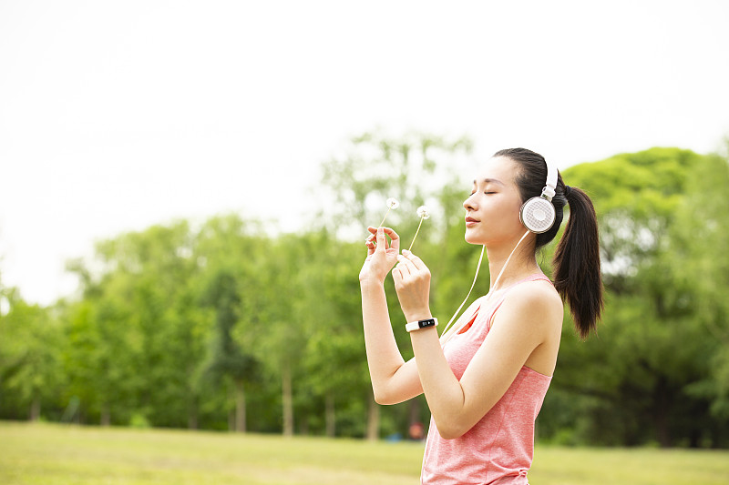 年轻女子戴耳机拿着蒲公英户外公园做运动图片下载