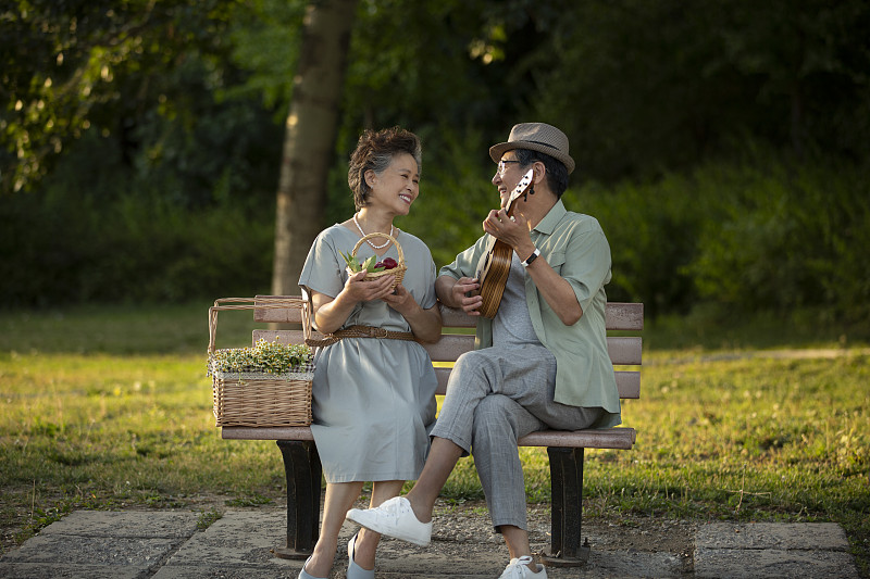 老年夫妻坐在公园长椅上野餐弹奏尤克里里琴图片下载