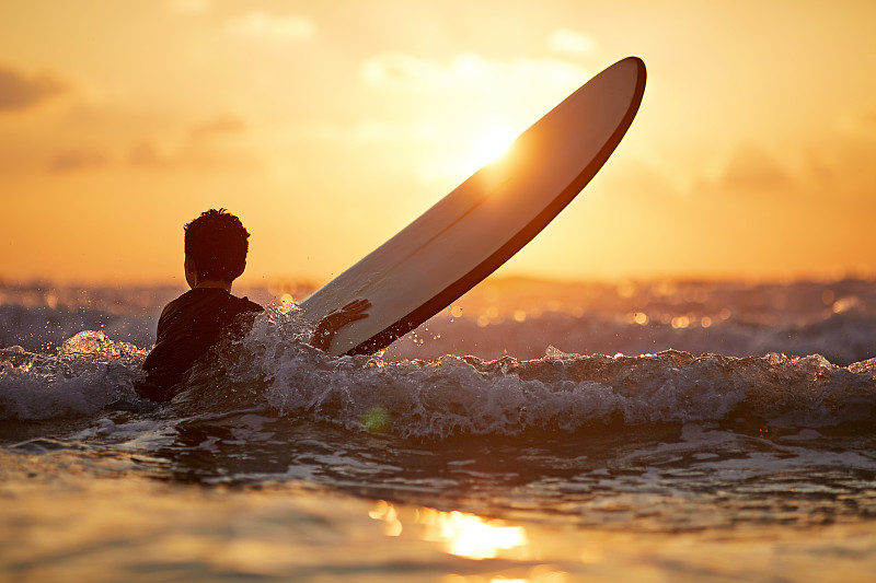 小男孩(10-11)在日落的海浪冲浪的后视镜图片素材