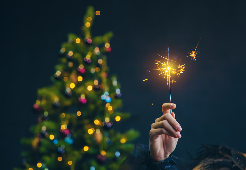 近距离观看女人的手拿着发光的装饰圣诞树在夜空。图片下载