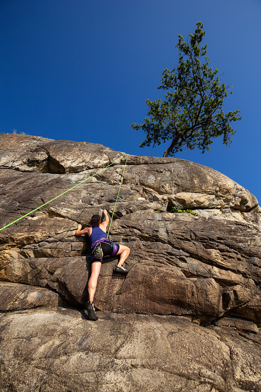 低角度的女人爬在岩石上对清澈的蓝色天空图片下载