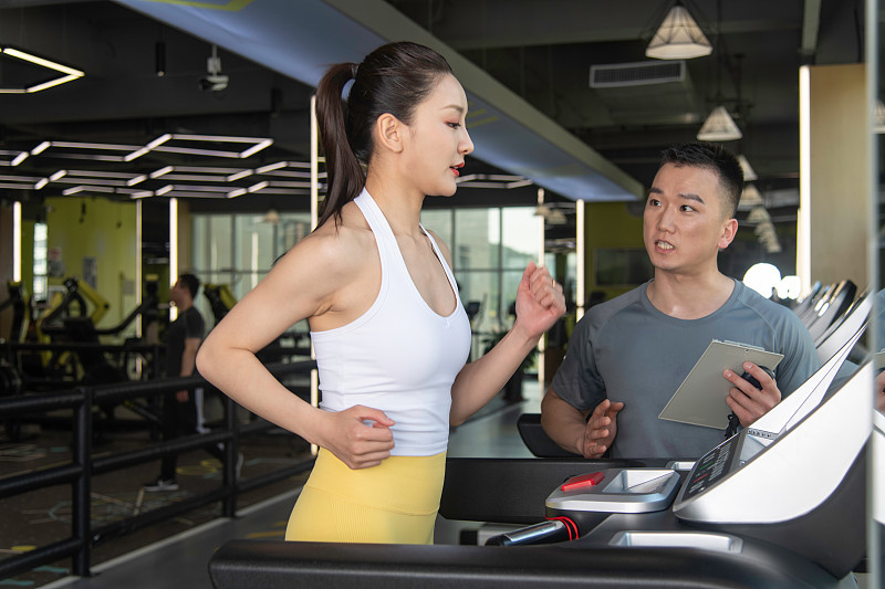 正在健身的年轻女性和男性，在健身房使用跑步机锻炼。专业健身教练评测、指导和辅助训练、学习和交流图片下载