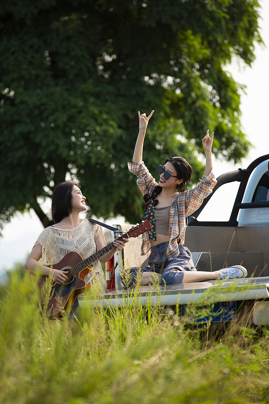 年轻闺蜜户外旅行坐在皮卡车里弹奏吉他唱歌跳舞玩耍图片下载