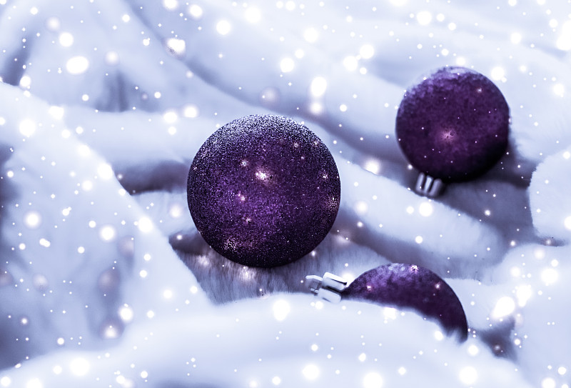 紫色圣诞装饰物在毛茸茸的毛皮上，雪花闪闪发光，奢侈图片下载