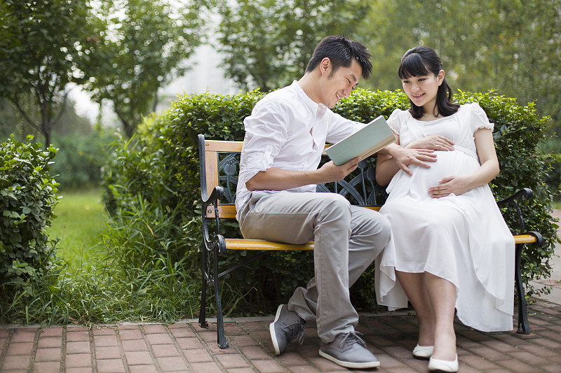 年轻男士给怀孕的妻子读书图片素材
