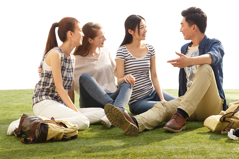 年轻的大学生坐在草地上闲谈图片下载