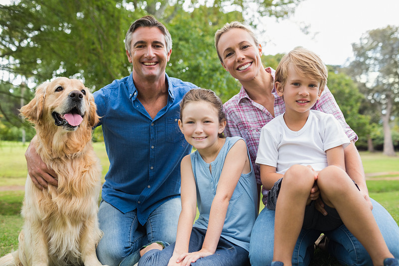 在一个阳光明媚的日子里，幸福的家庭和他们的狗对着镜头微笑图片下载