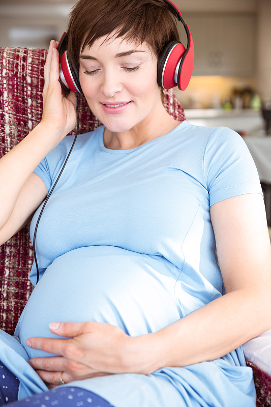 一名孕妇在起居室里戴着耳机图片下载