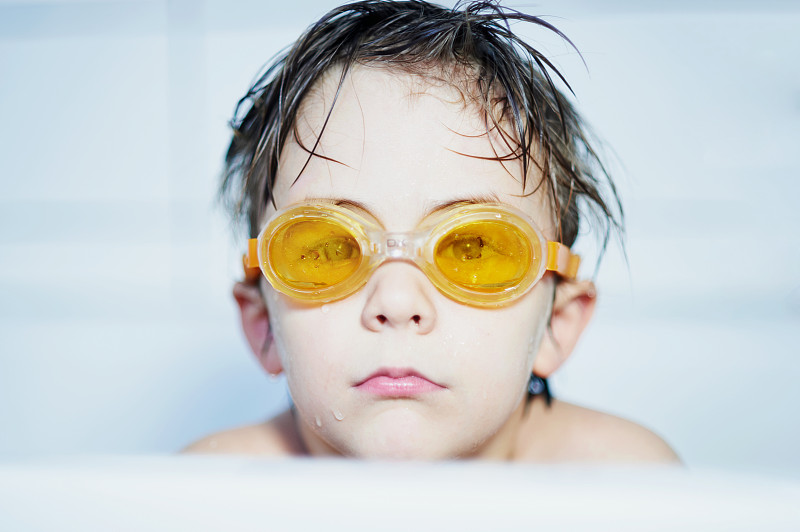 男孩的肖像(8-9)坐在浴缸与黄色泳镜图片素材