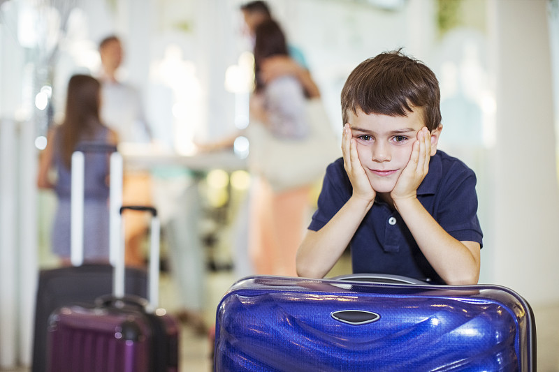 在酒店大厅里，一个沉思的男孩倚在行李箱上的肖像图片素材