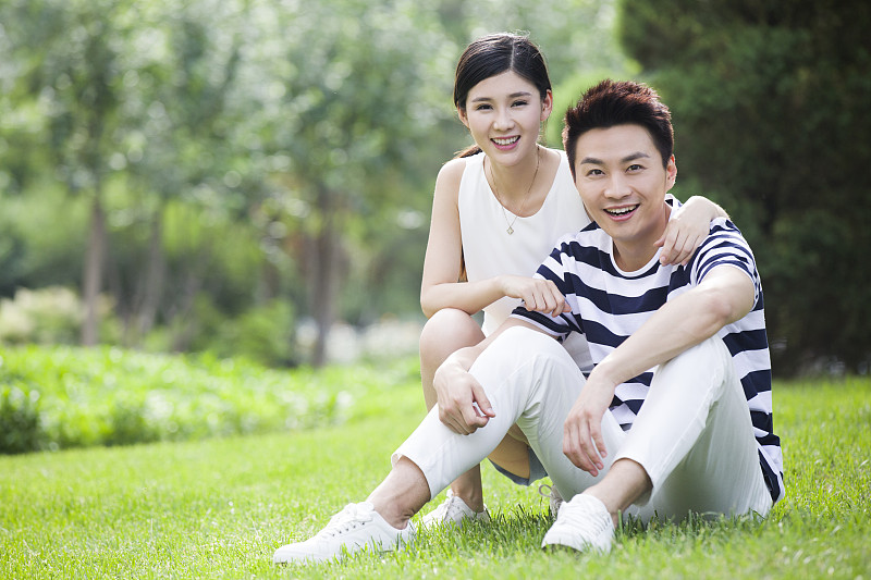 快乐的年轻情侣坐在草地上图片下载