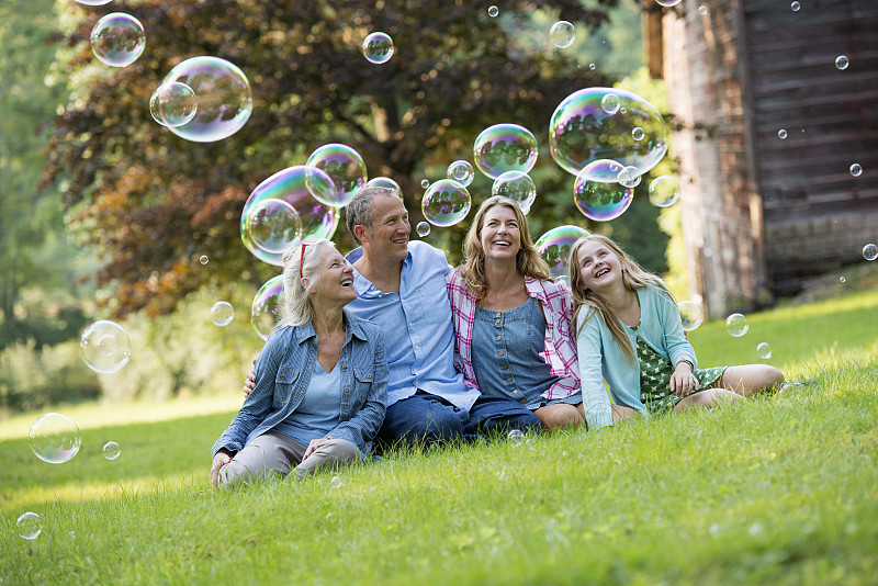一家人坐在酒吧外的草地上，吹着泡泡，笑着。图片素材