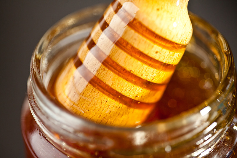 蜂蜜舀出一个罐子，以黑色为背景图片下载