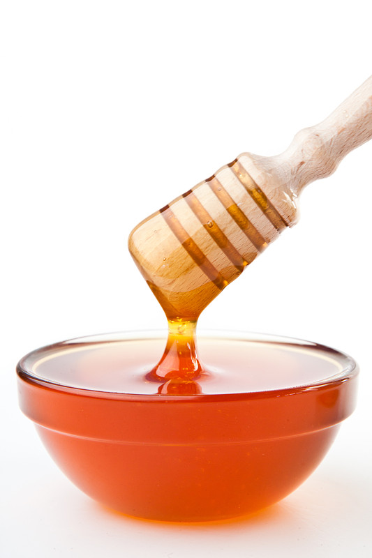 在白色背景下，蜂蜜勺放在蜂蜜碗上图片素材