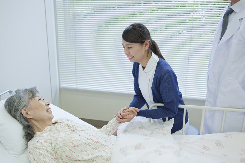 日本本州神奈川县，一位老年妇女躺在床上与护士和医生交谈图片下载