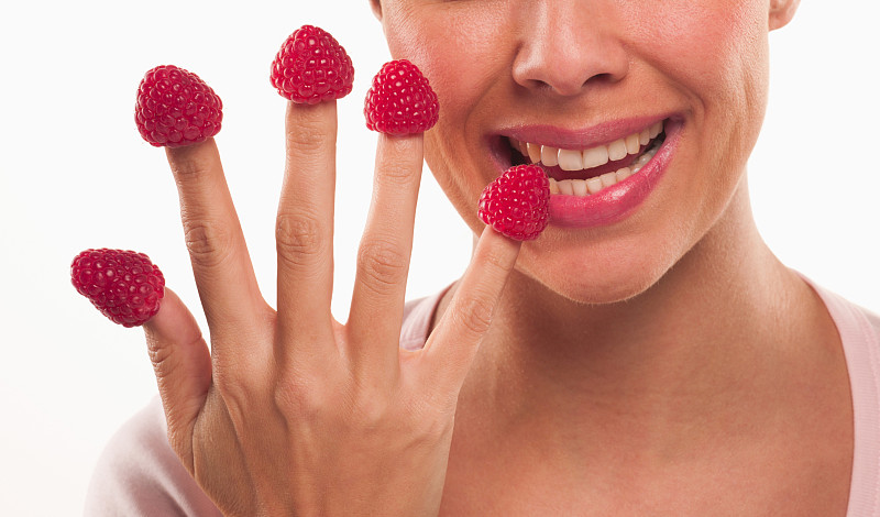 近距离的女人咬树莓的指尖图片素材