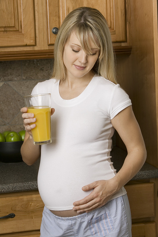 一个孕妇在厨房里拿着一杯橙汁图片下载