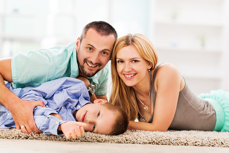 幸福的父母和他们的儿子在地毯上放松。图片下载