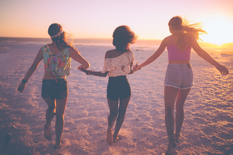 日落时分，在海滩上牵着手跑步的女性朋友们图片素材