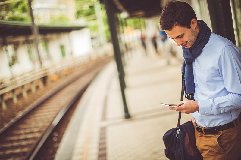 一个年轻人在火车站用智能手机图片下载