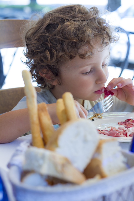 饥饿的孩子用叉子和手吃饭图片下载