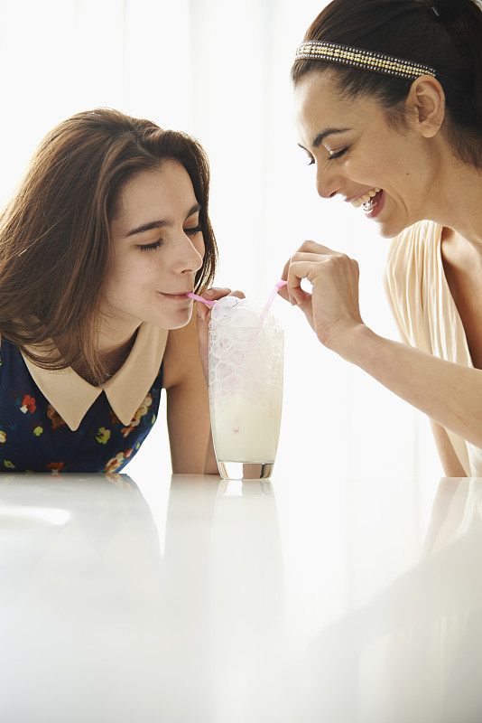 母亲和女儿在餐桌上一起在牛奶中吹泡泡图片下载