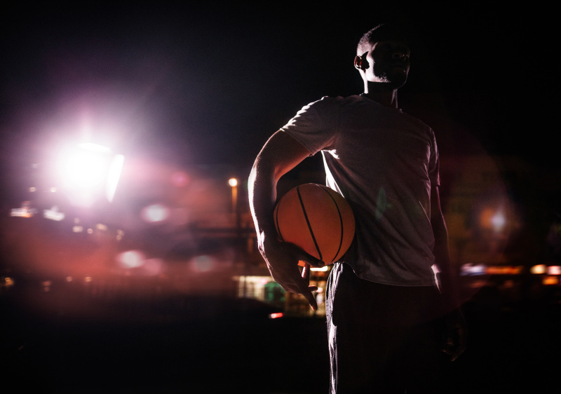 男子篮球运动员抱球在臀部在晚上图片下载