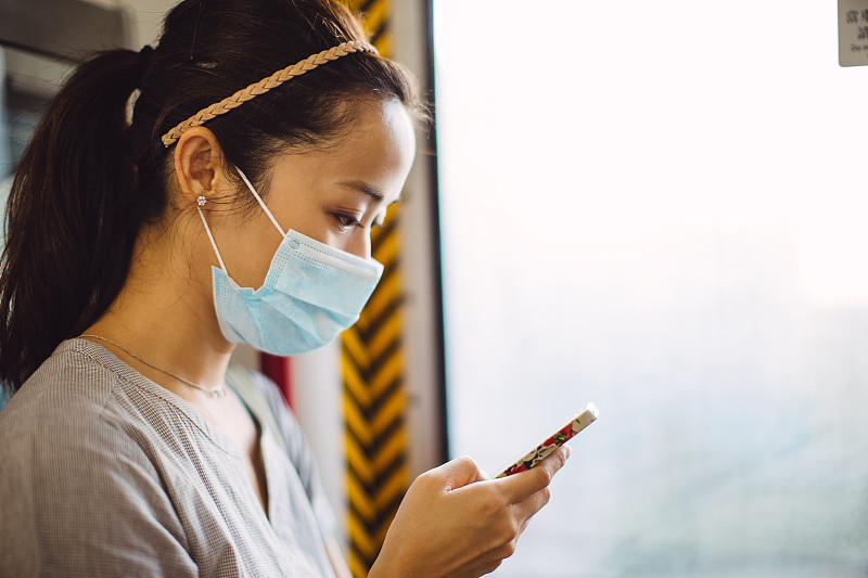 年轻女子戴着口罩在火车上使用智能手机图片下载