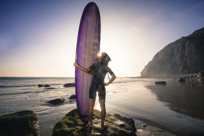 日落时分，一名亚洲女冲浪者站在她的冲浪板前望向加州的大海图片下载