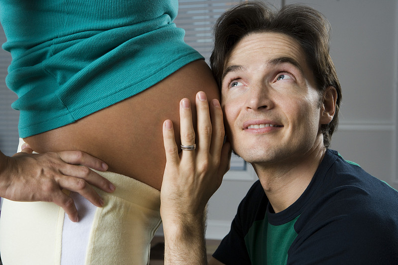 一个男人把他的耳朵贴在一个孕妇的肚子上的特写图片下载