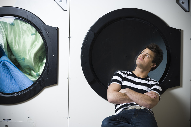 男人坐在洗衣店双臂交叉看着烘干机图片下载