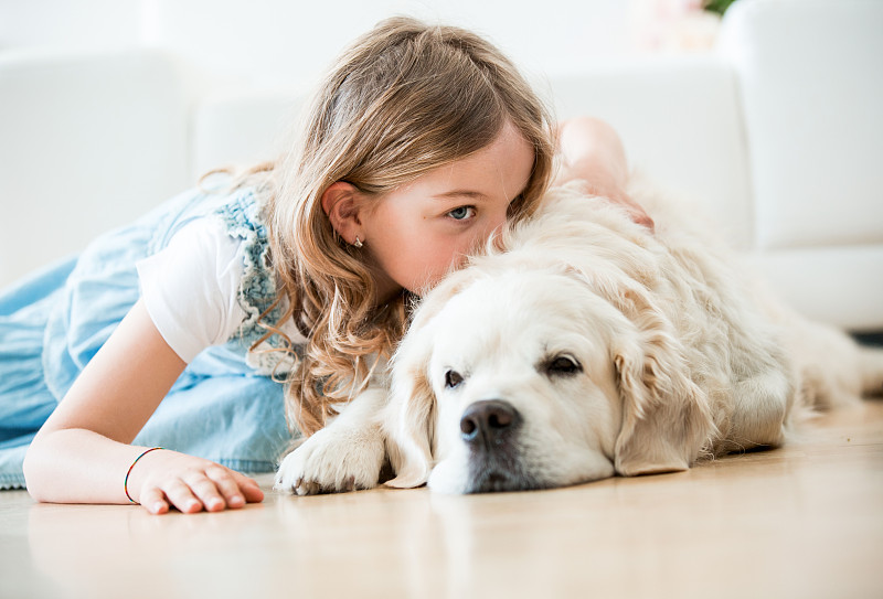 小女孩抱着她的狗，躺在地板上图片下载