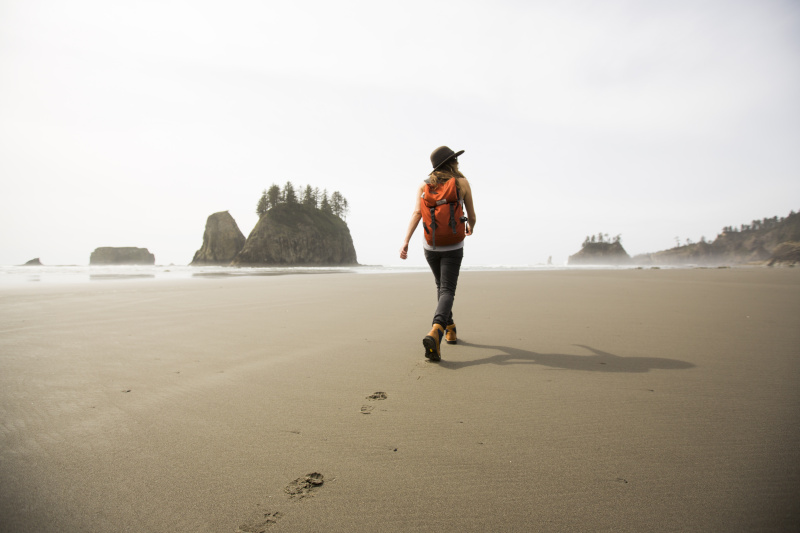 在偏远的海滩上徒步旅行的女人。图片下载