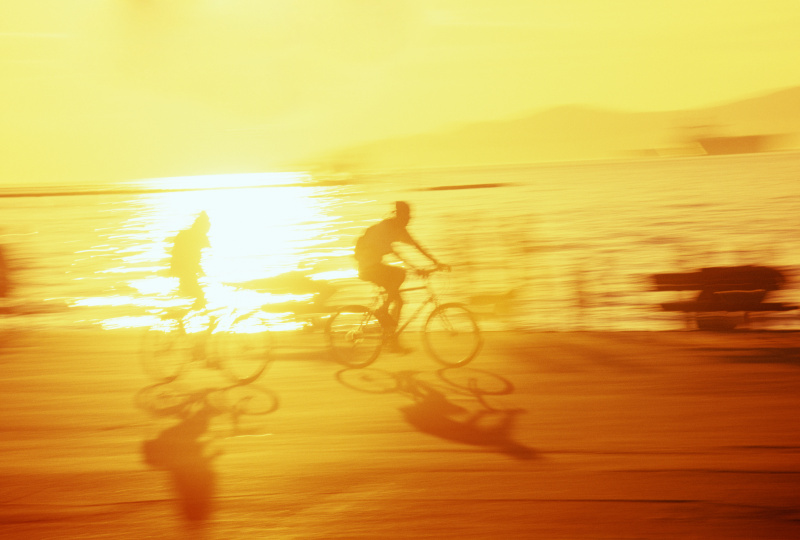 两个人在海滩上骑自行车，耀眼的阳光反射在海里图片下载